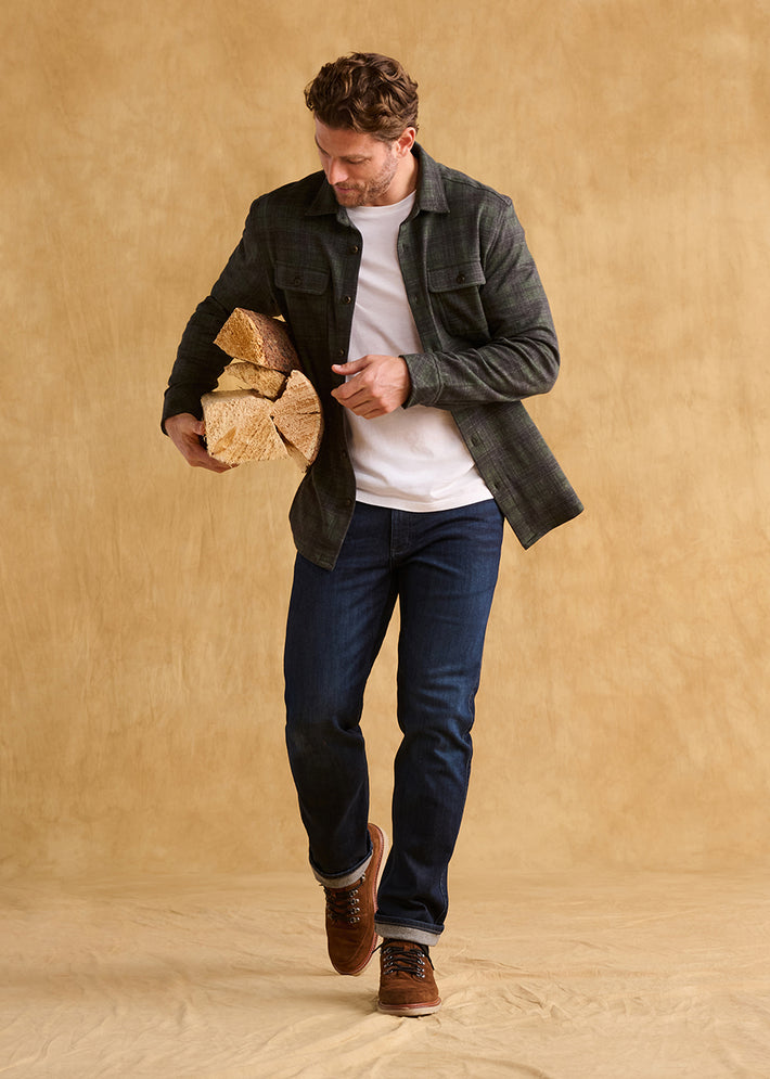 Man holding firewood against a beige background wearing Duer performance denim jeans