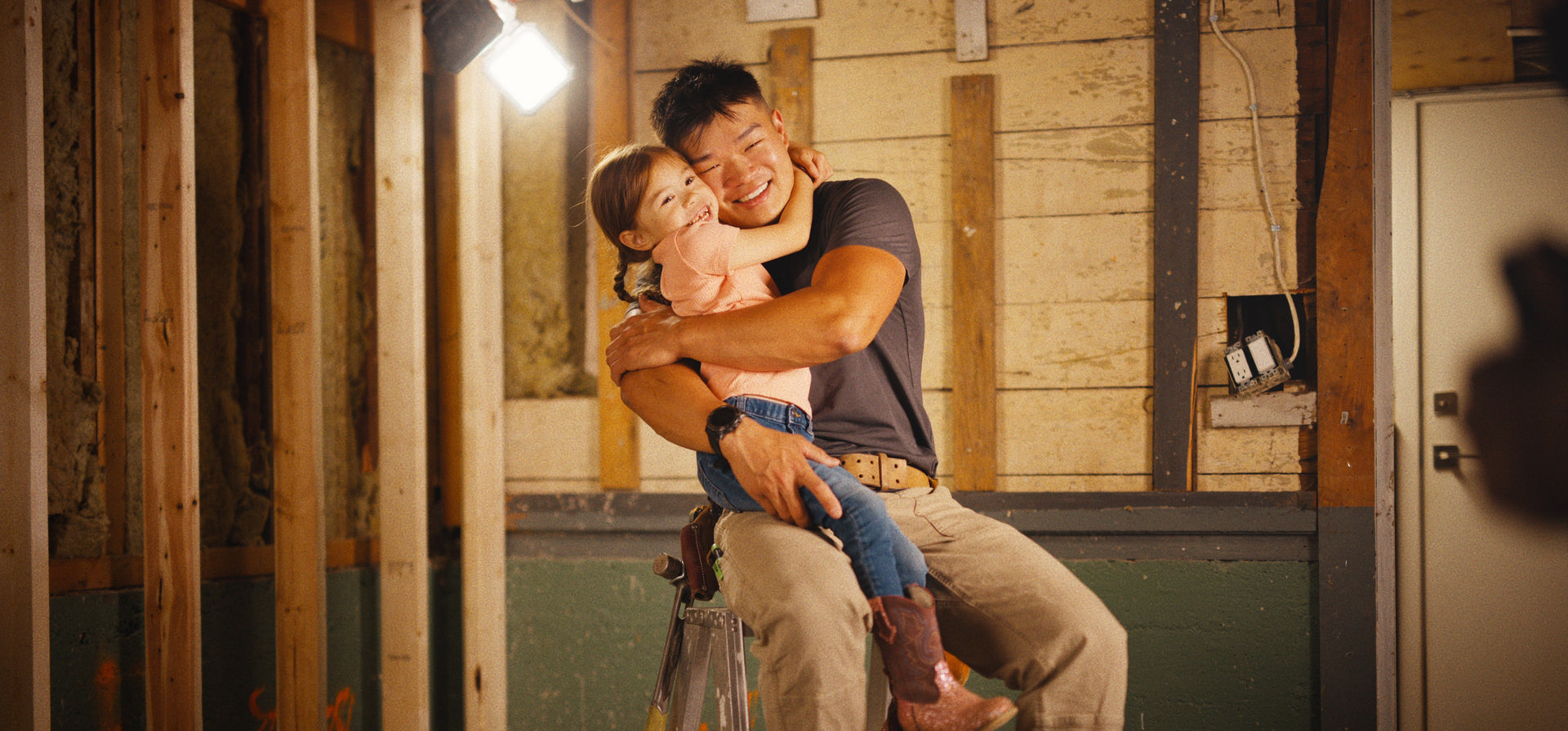 Man lifting a child on a ladder in an unfinished room