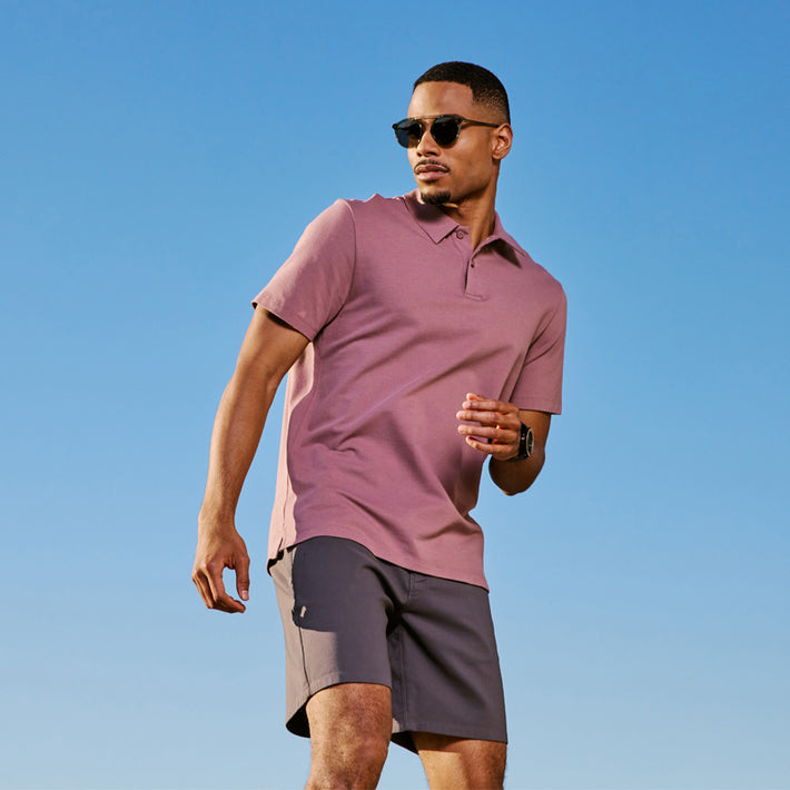 Man wearing a pink polo shirt and DUER gray shorts against a clear blue sky