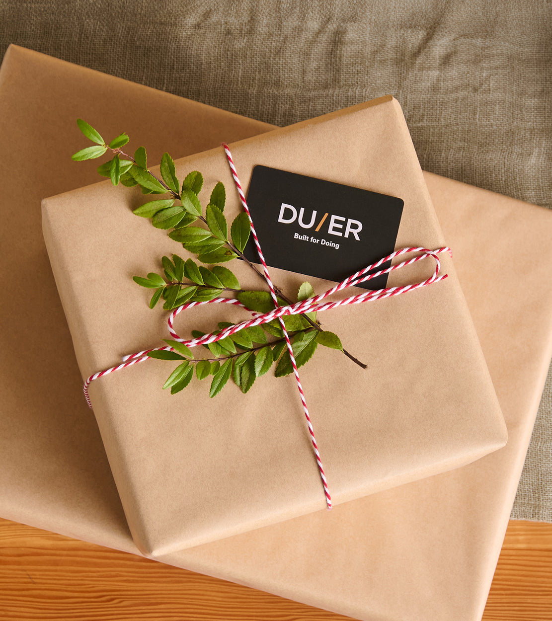 Gift wrapped in brown paper with a Duer gift card and green leaves on a wooden surface