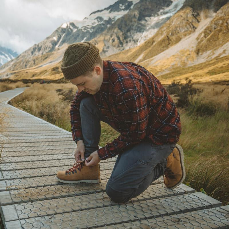 A man wearing Adventure Pants tying his shoes on a wooden pathway in the mountains.